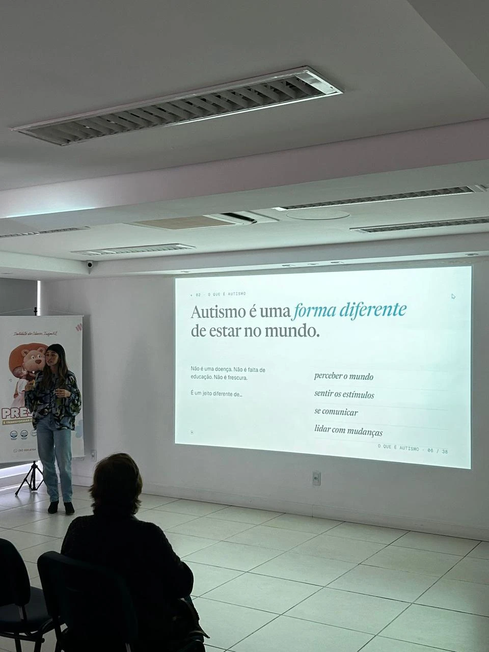 Betina Binatti em palestra, ao lado do slide: Autismo é uma forma diferente de estar no mundo.